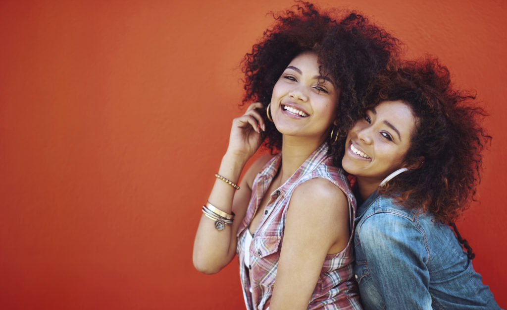 Shot of two young friends posing against a red background